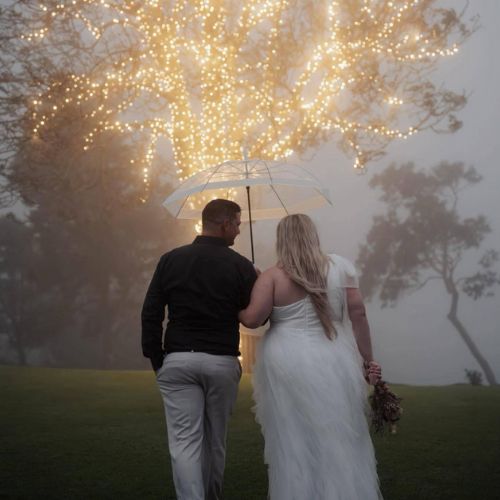 Bride and groom walk hand-in-hand through misty grounds at Western Ridge, illuminated by a magical tree wrapped in fairy lights.