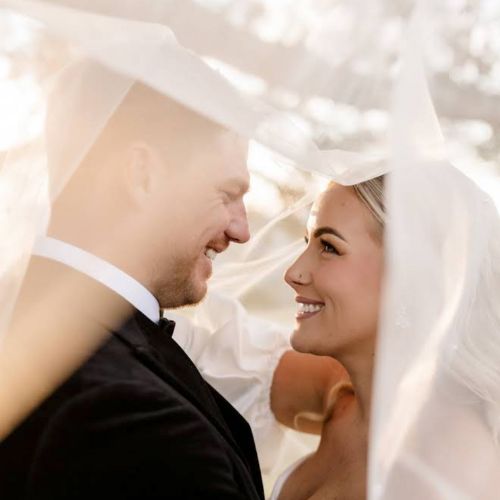 Bride and groom smiling at each other under a wedding veil at Western Ridge.